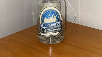 A lamp with a clear bottle base, a grey lampshade, and a label reading "HELLSMOUTH VANILLA RUM LIQUEUR 25% VOL 500 ML".