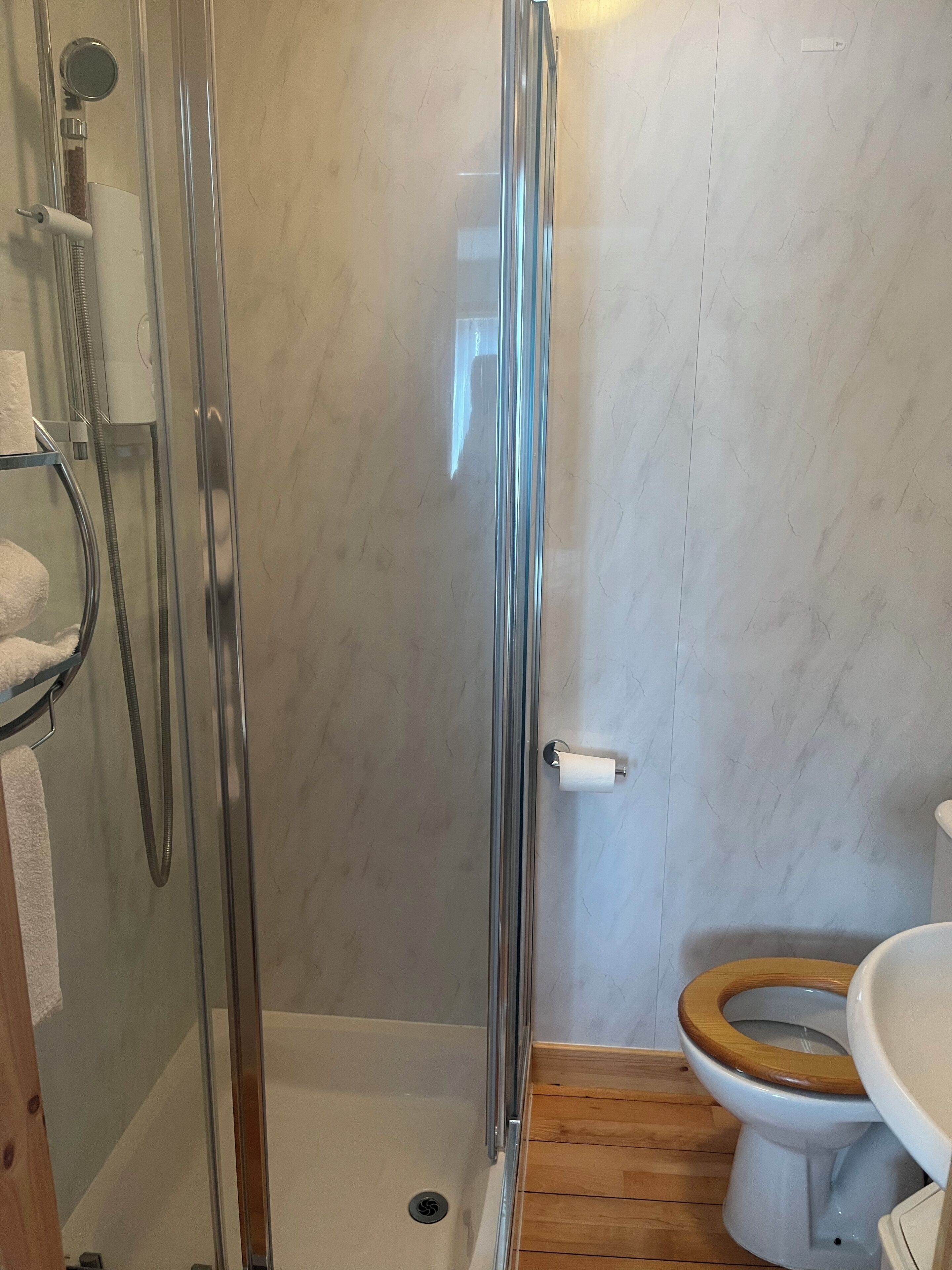 Een badkamer met een glazen douchecabine, een houten toiletbril en een witte wastafel.