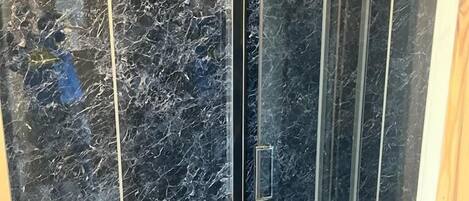 A shower with a glass door and a marble wall.