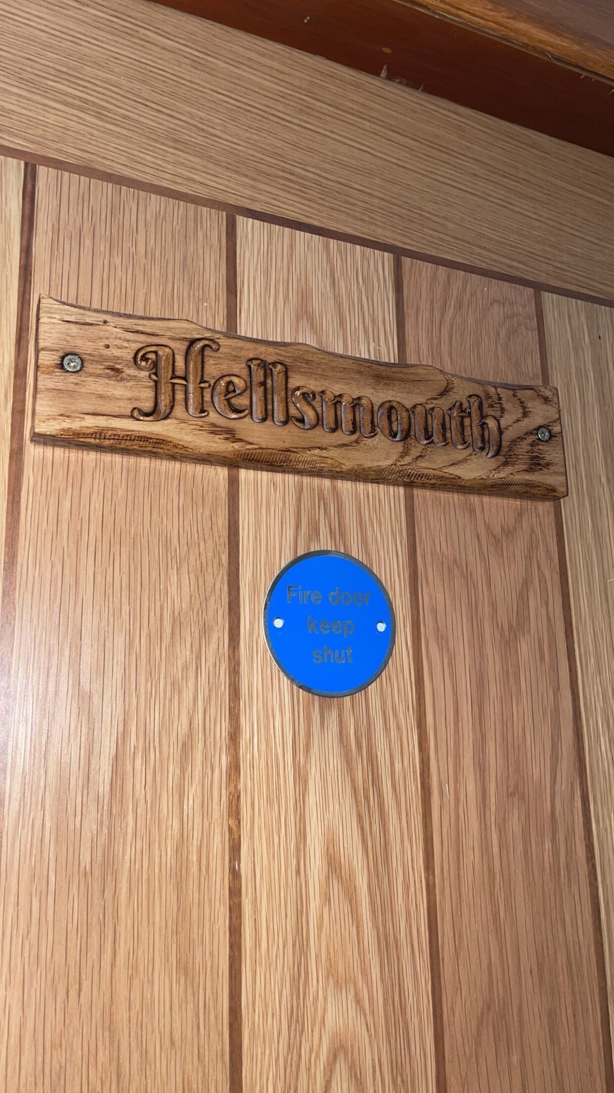 A wooden sign with the name "Hellsmith" and a blue circular sign below it that reads "Fire door keep shut."