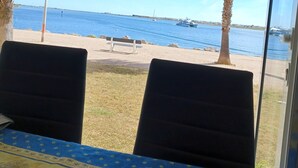 Une pièce avec vue sur la mer, deux chaises, une table recouverte d’une nappe bleue et un palmier à l’extérieur.