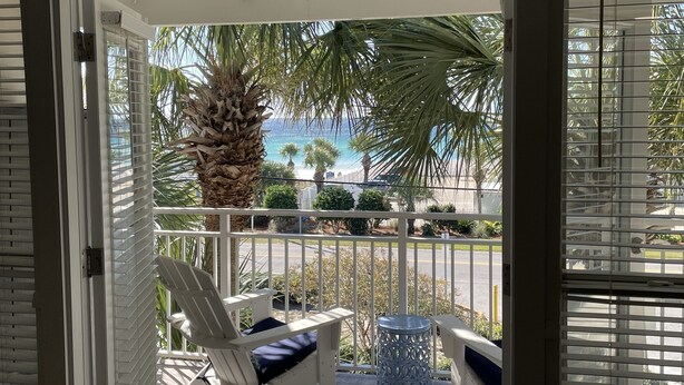 Ein Balkon mit einem weißen Stuhl und einem kleinen Tisch, mit Blick auf eine Palme und das Meer.