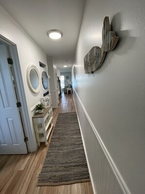 Käytävän lattia on tehty puusta, seinät ovat valkoiset ja siellä on matto. Siellä on myös kaksi pyöreää peiliä ja pieni pöytä, jonka päällä on kasvi.