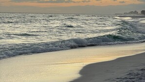 Ein Strand mit Wellen und einer Stadtansicht in der Ferne.