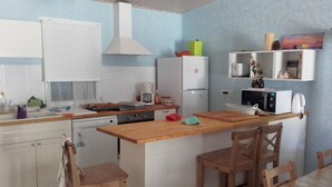 Une cuisine compacte avec des meubles blancs, un plan de travail en bois, un four à micro-ondes encastré et un petit réfrigérateur.