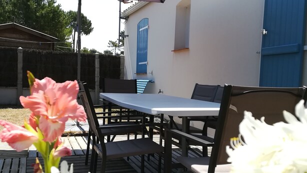 Une terrasse extérieure avec une table et des chaises, un grand parasol et un mur avec une porte bleue.