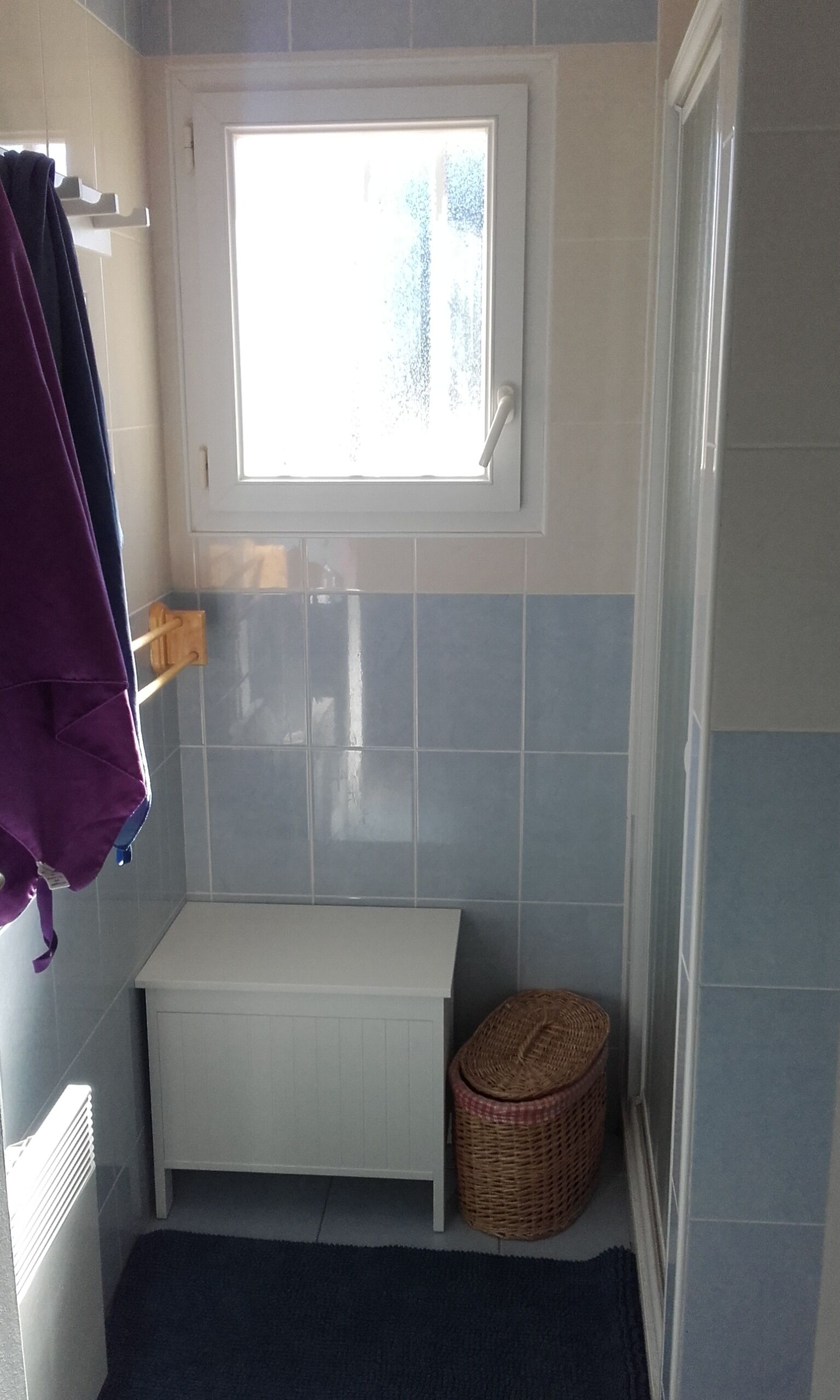 A small bathroom with a window, a bench, and a wicker basket.