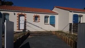 Un immeuble résidentiel avec un toit recouvert de tuiles rouges, des murs blancs et des volets bleus.