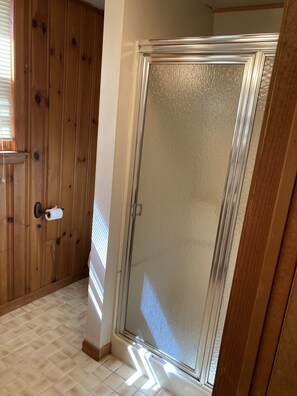 Shower area features a large glass door with a metallic frame and handle, adjacent to a window with horizontal blinds.