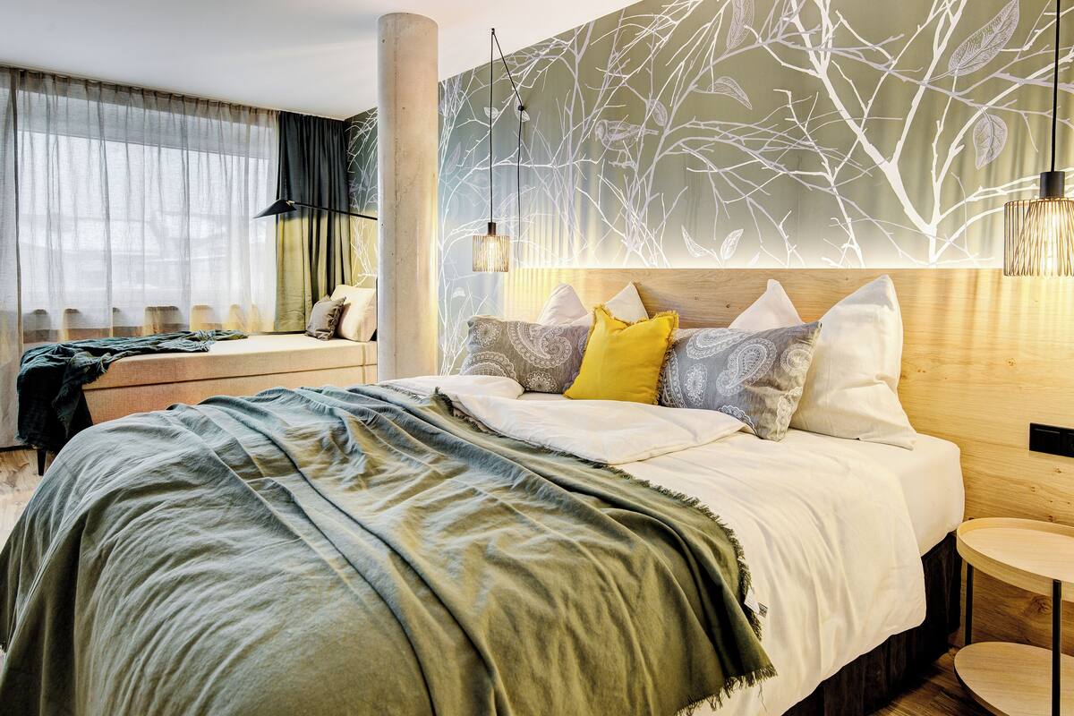 A modern hotel room with a large bed, a wooden headboard, and a wall with a tree branch pattern.