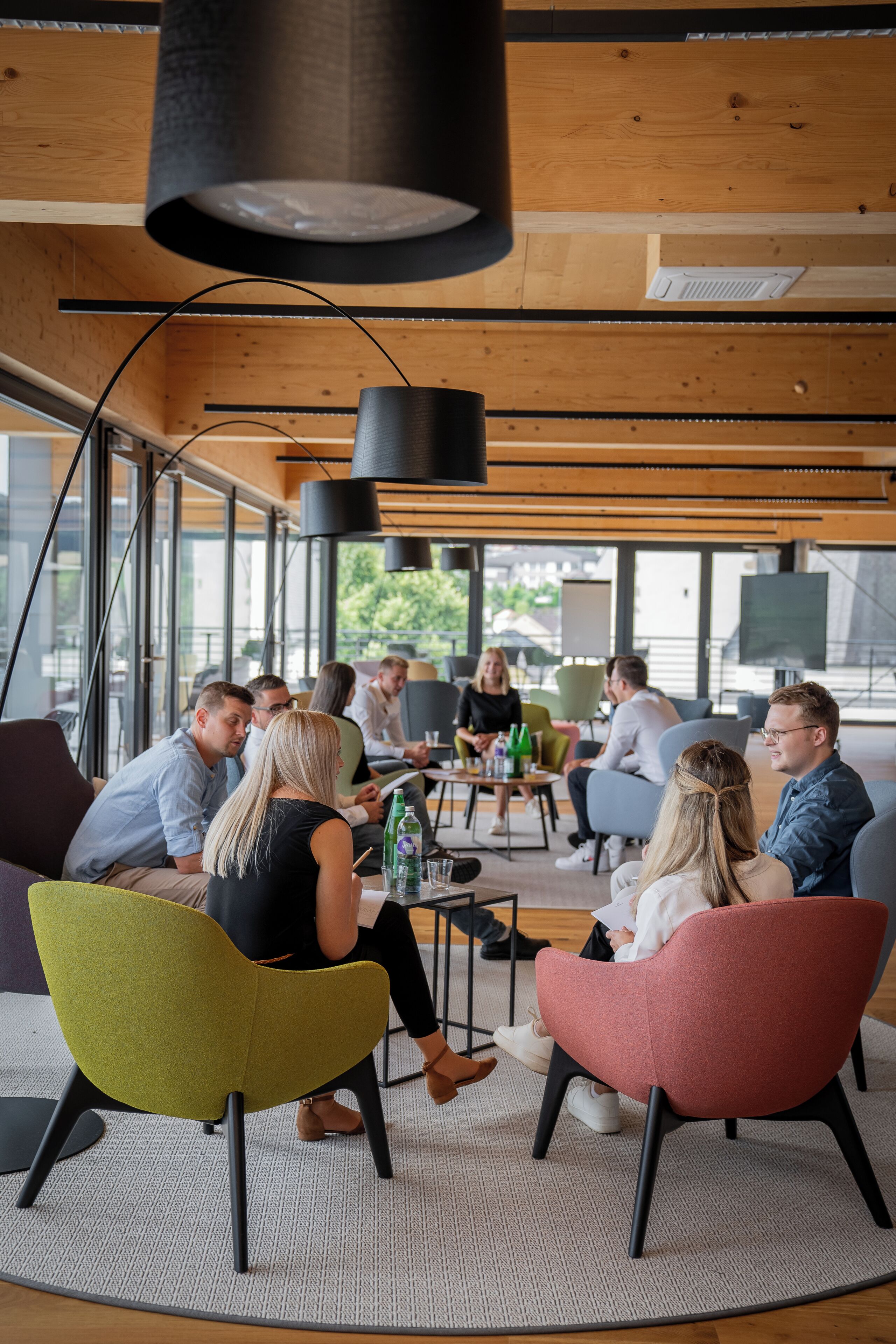 A modern meeting room with wooden ceilings, large windows, and colorful chairs.