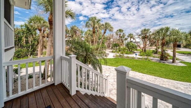 A wooden porch with white railings overlooking a landscaped garden with palm trees and a clear sky. - Sanibel Home ready for rentals ! (Sanibel)