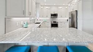 A modern kitchen with white cabinets, a granite countertop, a stainless steel refrigerator, and a built-in oven. - Sanibel Home ready for rentals ! (Sanibel)