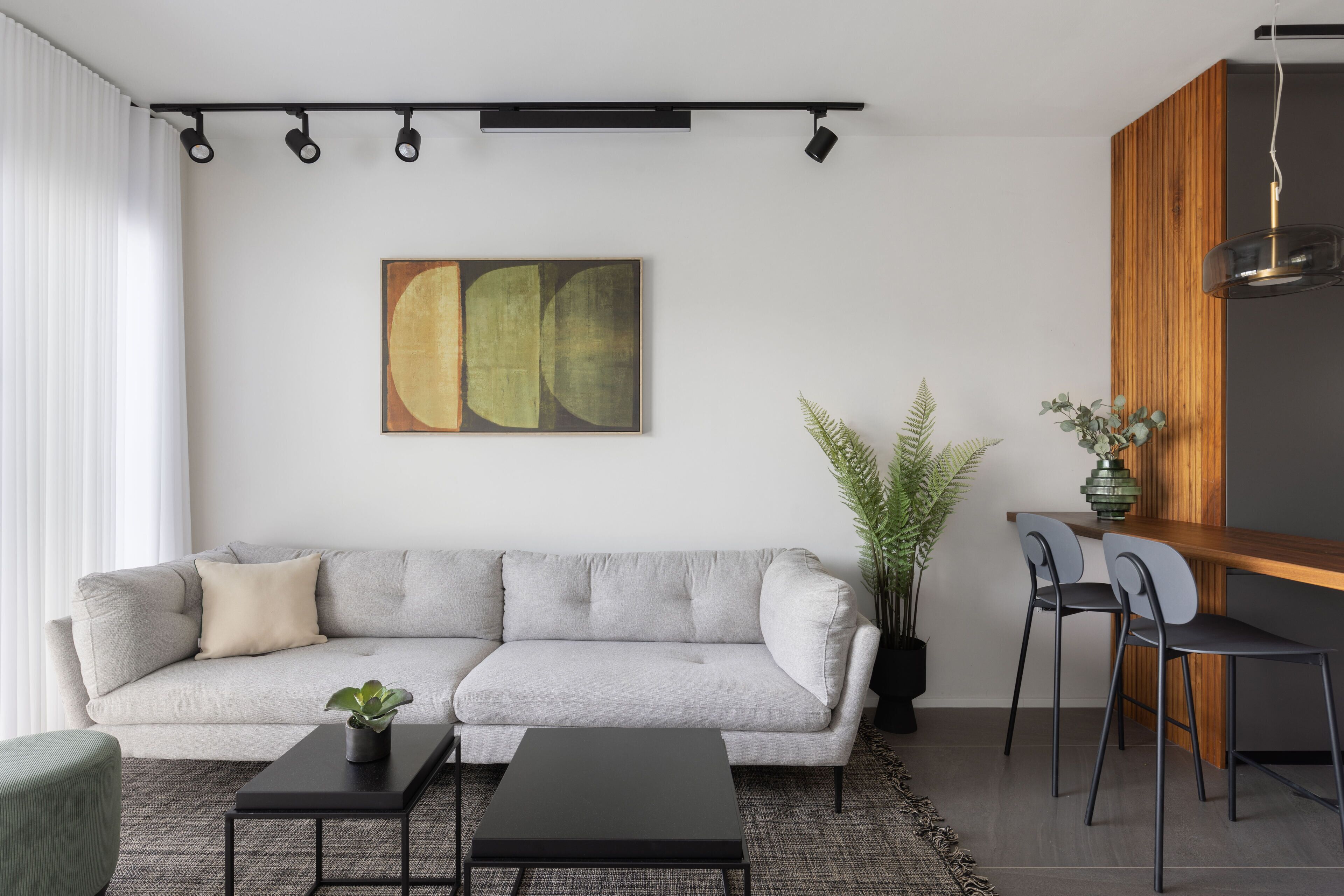 Een moderne woonkamer met een grijze bank, een zwarte salontafel en een eethoek met een houten tafel en twee stoelen.
