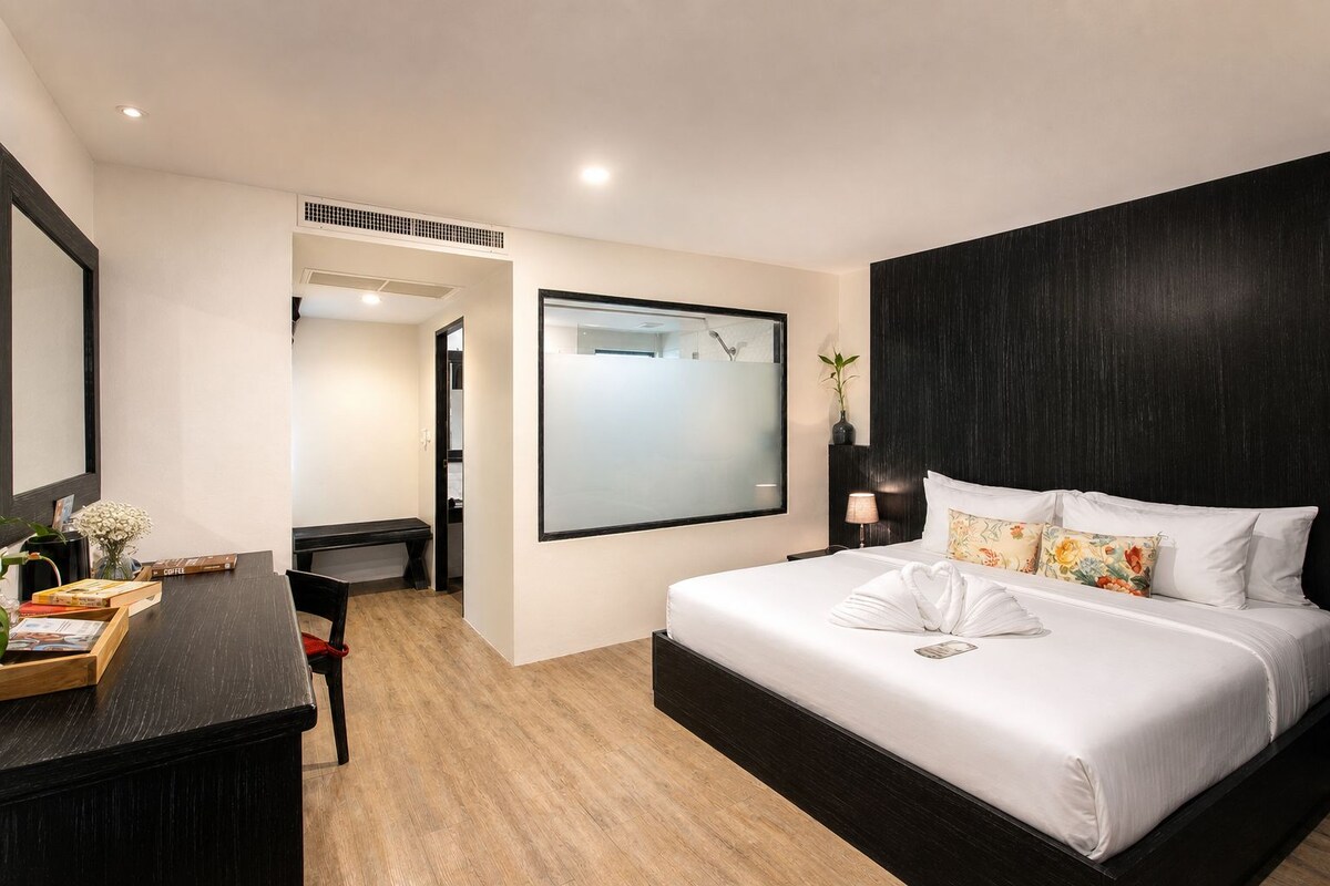 A modern hotel room with a large bed, a desk, and a shower area.