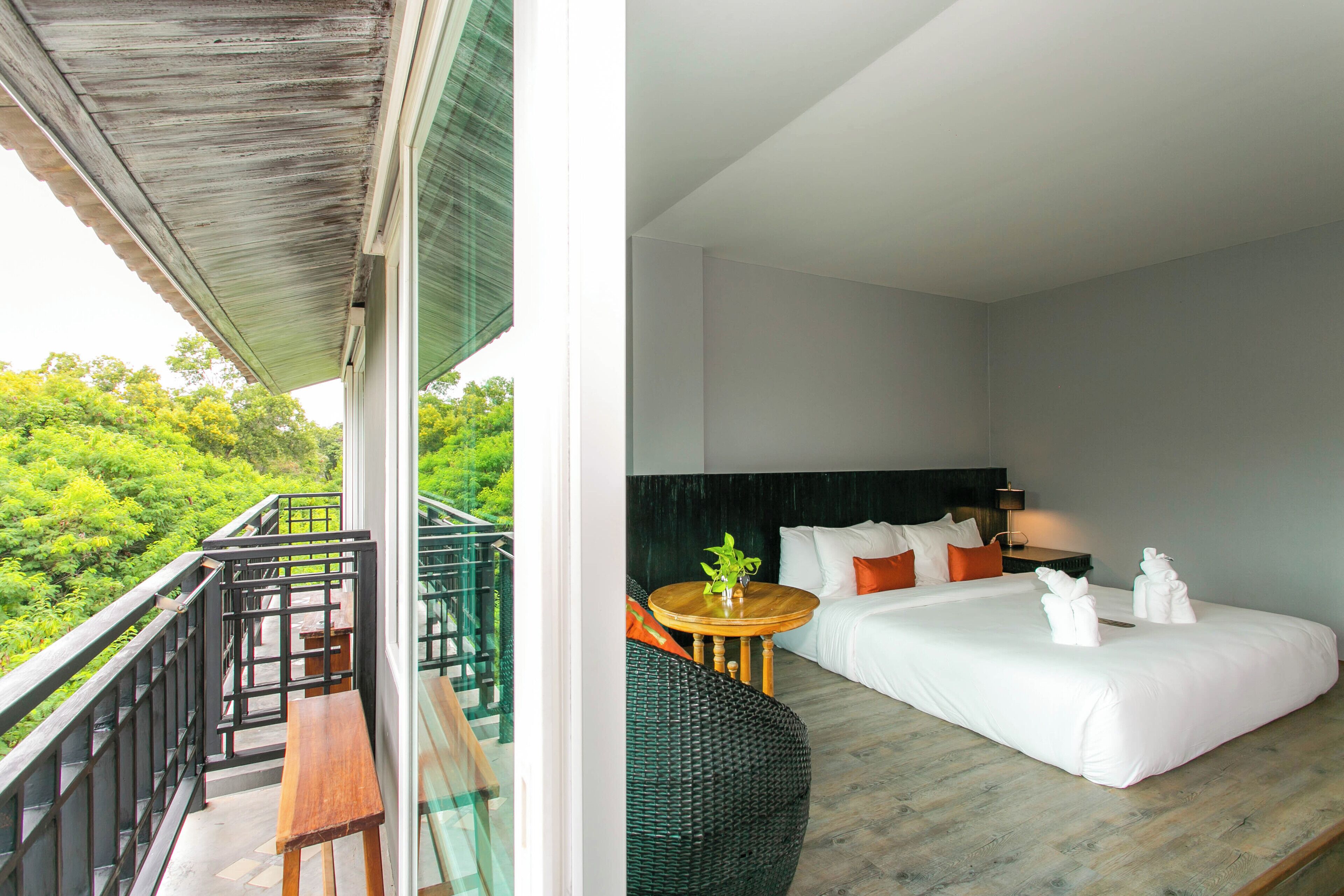 A hotel room with a balcony, a bed with white linens, a small round table, and a green wicker chair.