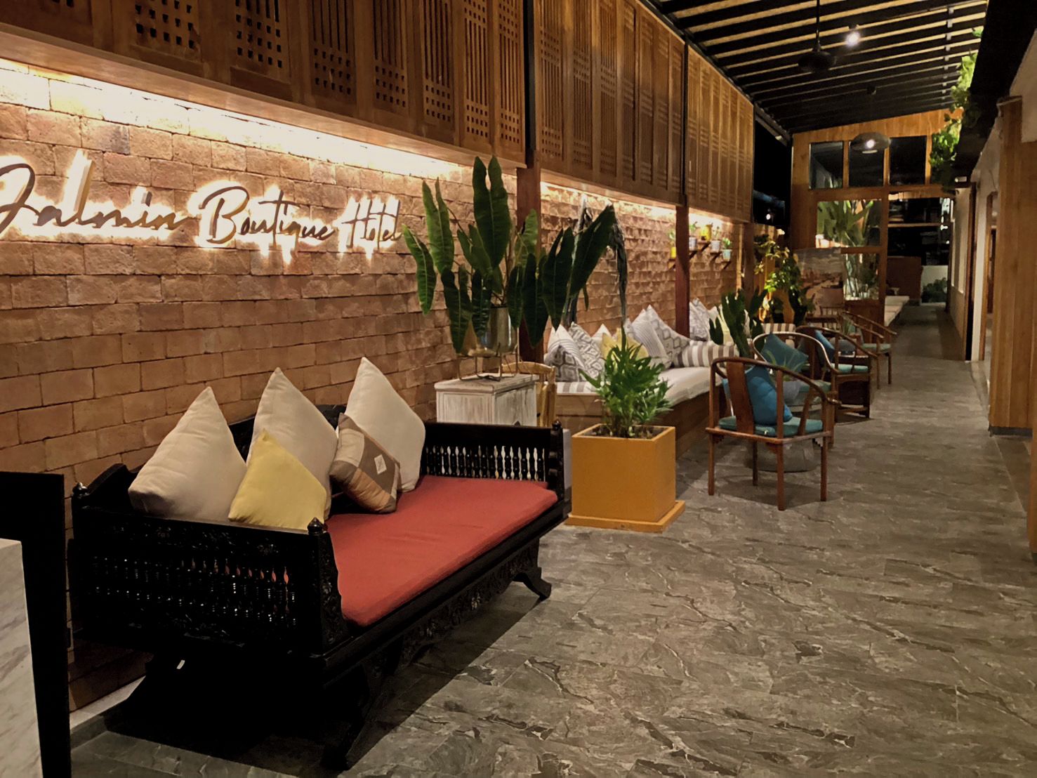 A lobby with a brick wall, a sofa with cushions, and a potted plant.