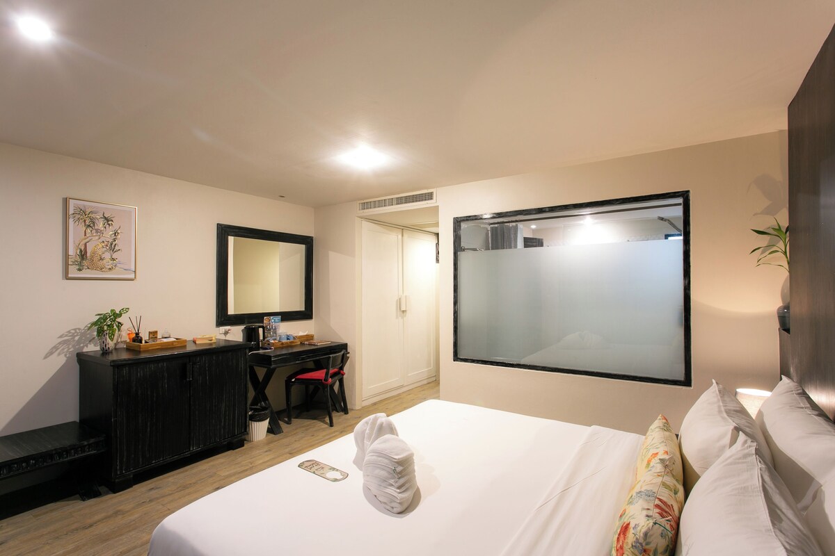 A hotel room with a bed, a desk, a chair, a wardrobe, and a large mirror.