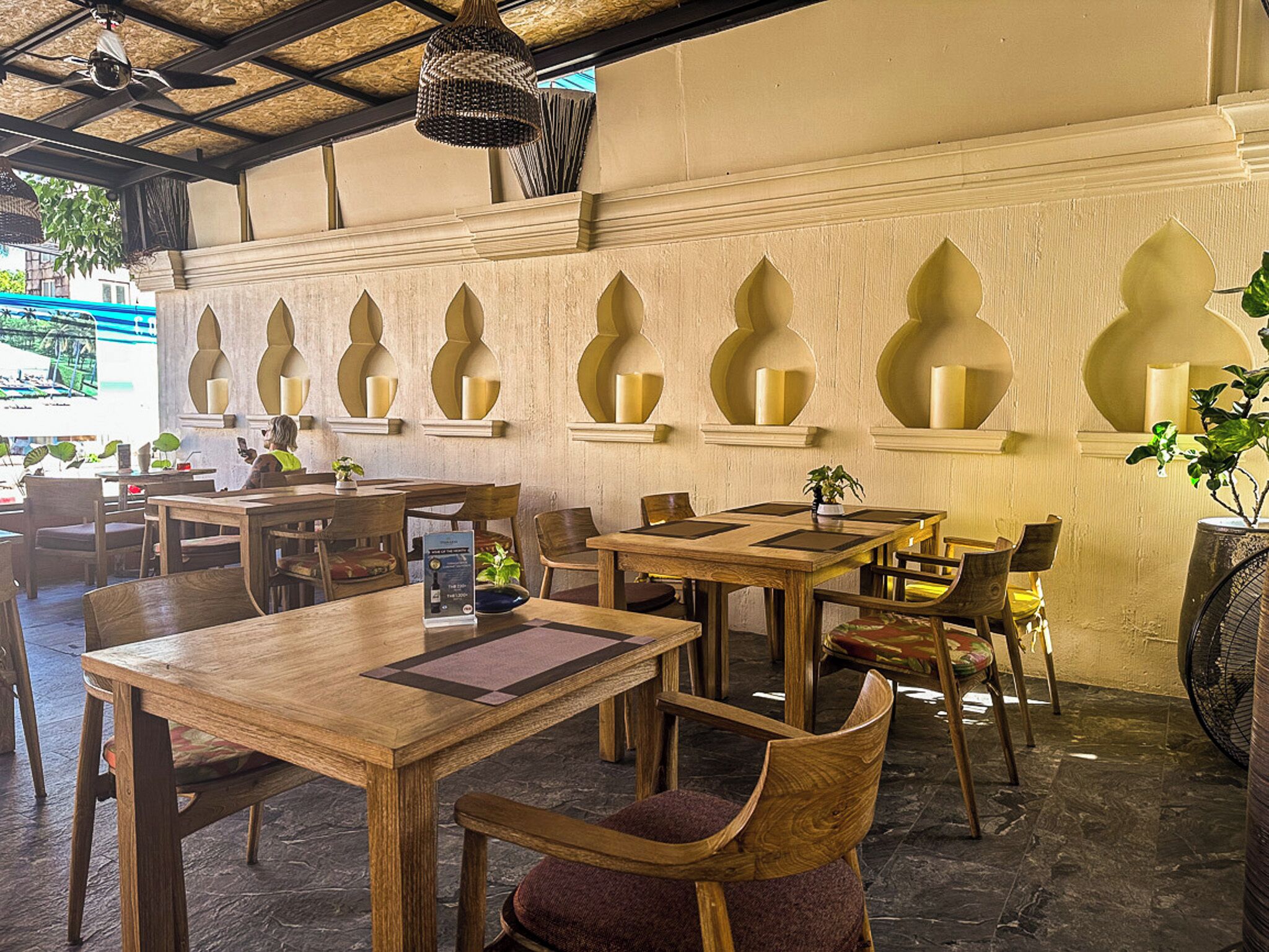 Un ristorante con tavoli e sedie di legno, applique decorative e una ventola a soffitto.