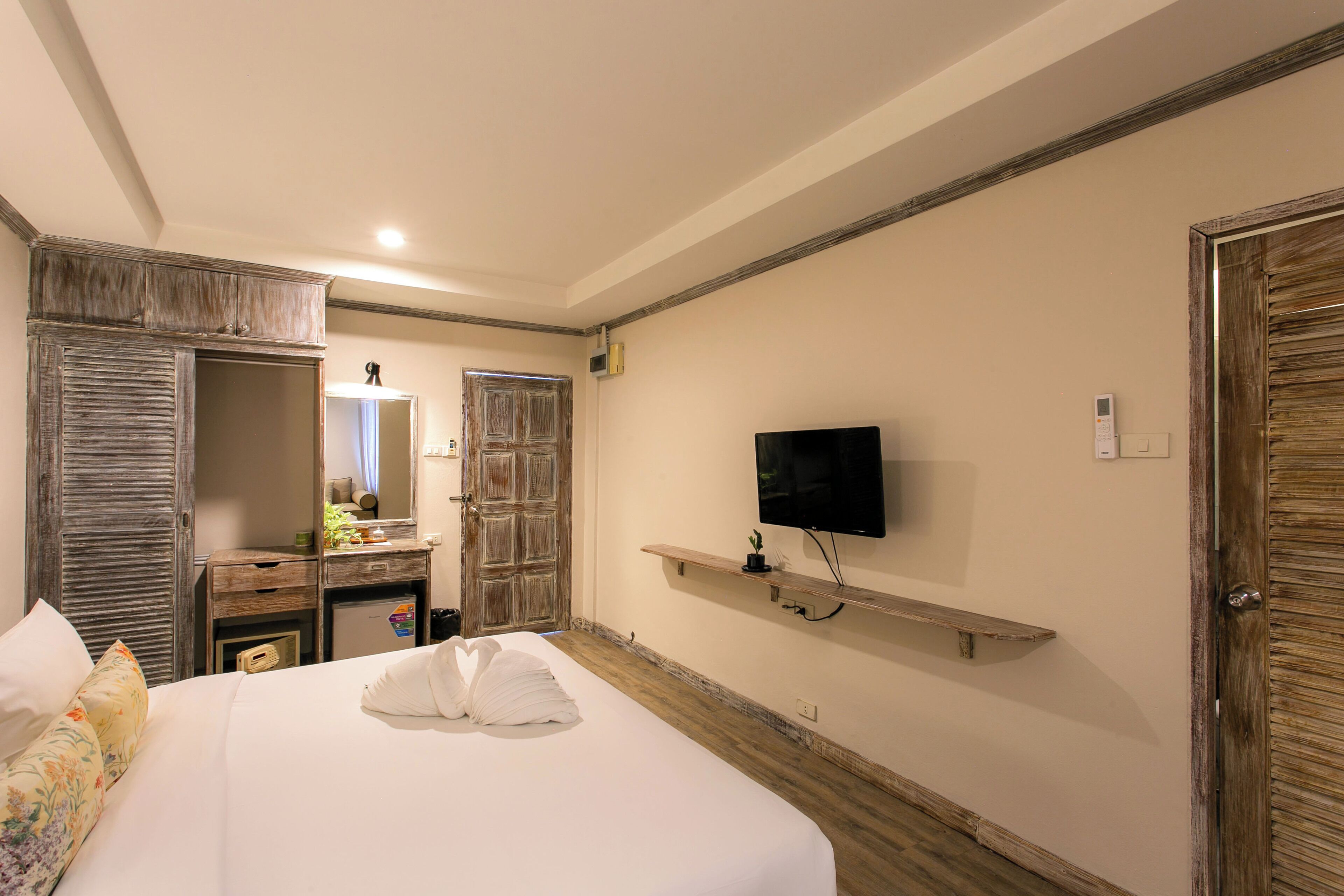 Ein Hotelzimmer mit Bett, Fernseher, Holzschrank, Spiegel und kleinem Schreibtisch.