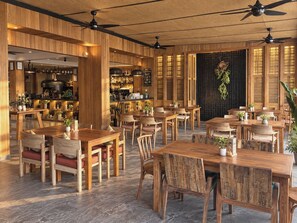 A restaurant with wooden furniture, ceiling fans, and a bar area. - JALMIN Samui Hotel (Koh Samui)