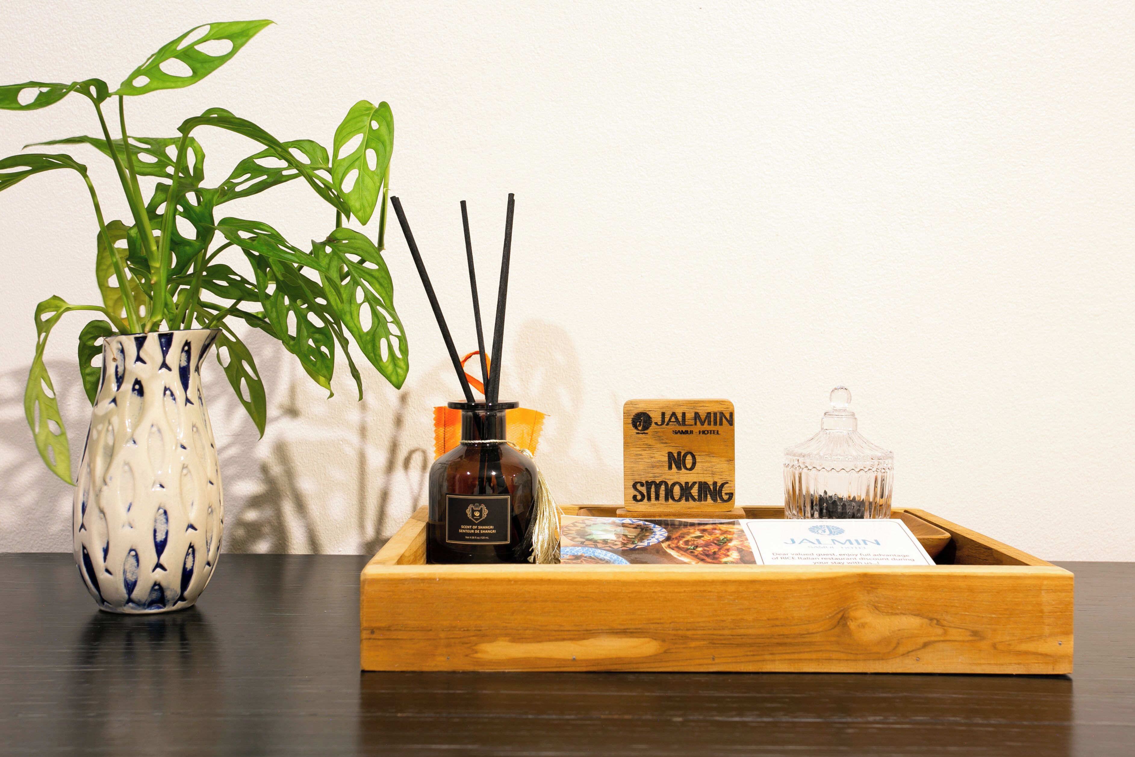 Una bandeja de madera con un cartel de 'No Smoking', una botella de JALMIN y un pequeño recipiente de vidrio.