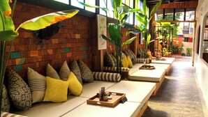 A row of white cushioned seating areas with patterned pillows, a wooden tray with items, and large green plants. - JALMIN Samui Hotel (Koh Samui)