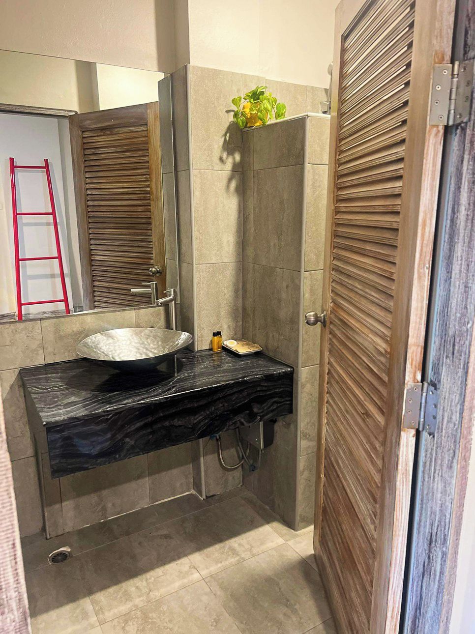 A bathroom with a black marble sink, a mirror, a towel rack, and a wooden door with a louvered design.