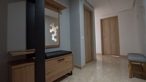 A hallway with a wooden bench, a wooden cabinet with a black countertop, and a wall-mounted hexagonal mirror. - Blue Paradise,a ray of Sunshine Between sea & Pool (Sonaba, Agadir)