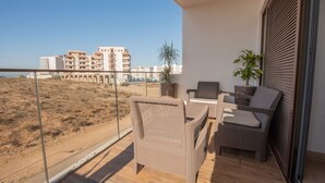 A balcony with wicker furniture, a potted plant, and a view of a beach and buildings. - Blue Paradise,a ray of Sunshine Between sea & Pool (Sonaba, Agadir)