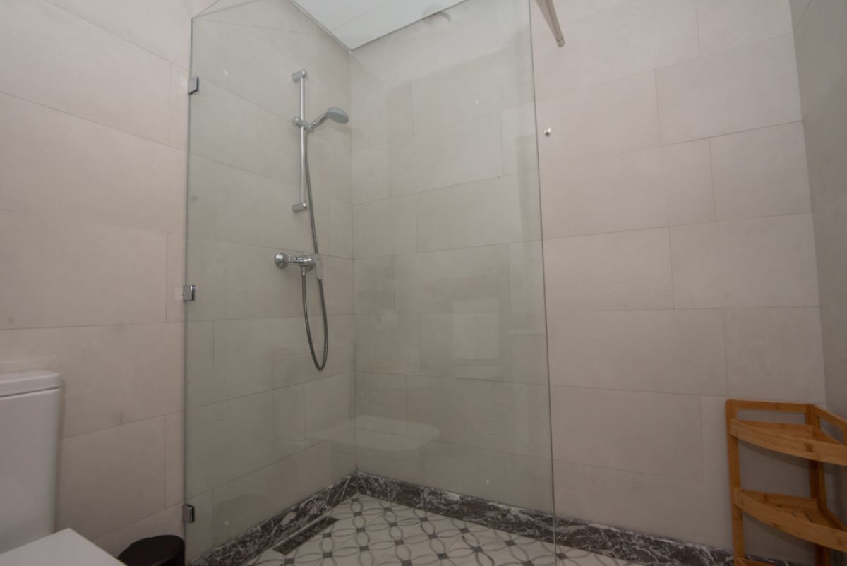 Een douchecabine van glas met een handdouche en een wandmengkraan.