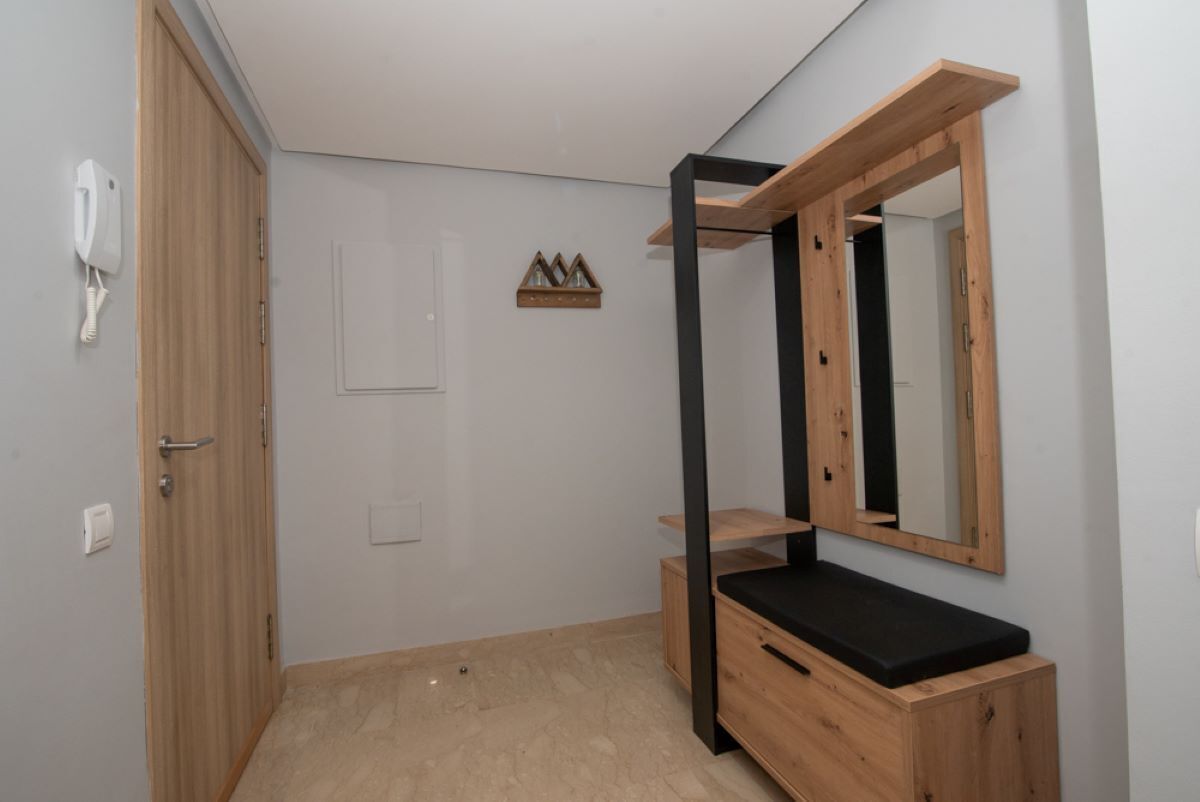 A small, modern bedroom with a wooden wardrobe, a black bench, and a mirror.