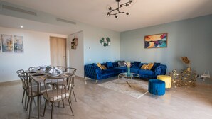 A modern living room with a blue sofa, a dining table set, and a chandelier. - Blue Paradise,a ray of Sunshine Between sea & Pool (Sonaba, Agadir)