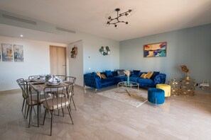 A modern living room with a blue sofa, a dining table set, and a chandelier.
