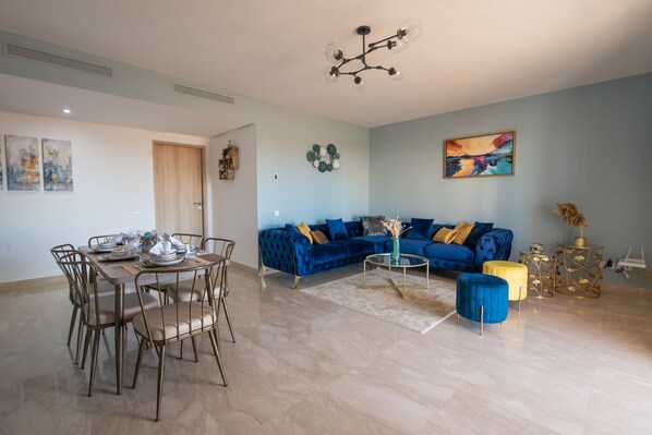 A modern living room with a blue sofa, a dining table set, and a chandelier. - Blue Paradise,a ray of Sunshine Between sea & Pool (Sonaba, Agadir)