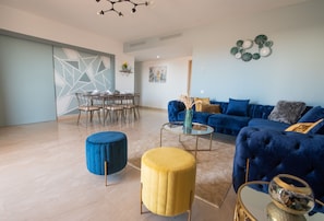 A modern living room with a blue sofa, a yellow ottoman, and a glass coffee table. - Blue Paradise,a ray of Sunshine Between sea & Pool (Sonaba, Agadir)