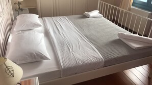A neatly made bed with white bedding, a bedside lamp, and a window with curtains. - PETRA Traditional HOUSE 2 (Ormos Korthiou)