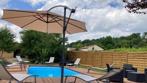 Eine Holzterrasse mit Pool, Liegestühlen und einem großen Sonnenschirm.