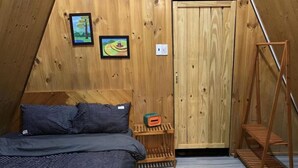 A triangular room with a bed, wooden walls, and a door. - Nha cua Nep (Dien Hong)