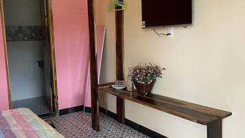 Ein Zimmer mit einem Bett, einer hölzernen Bank, einem an der Wand befestigten Fernseher und einer Tür zu einem Badezimmer.