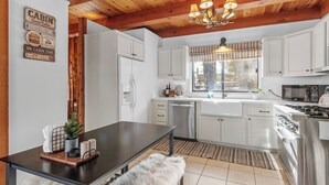 A modern kitchen with white cabinets, stainless steel appliances, a wooden ceiling, and a dining area with a bench. - The Lakehouse Cabin (Big Bear Lake)