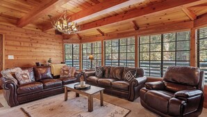 A log cabin interior with a brown leather sofa set, a wooden coffee table, and large windows with blinds. - The Lakehouse Cabin (Big Bear Lake)