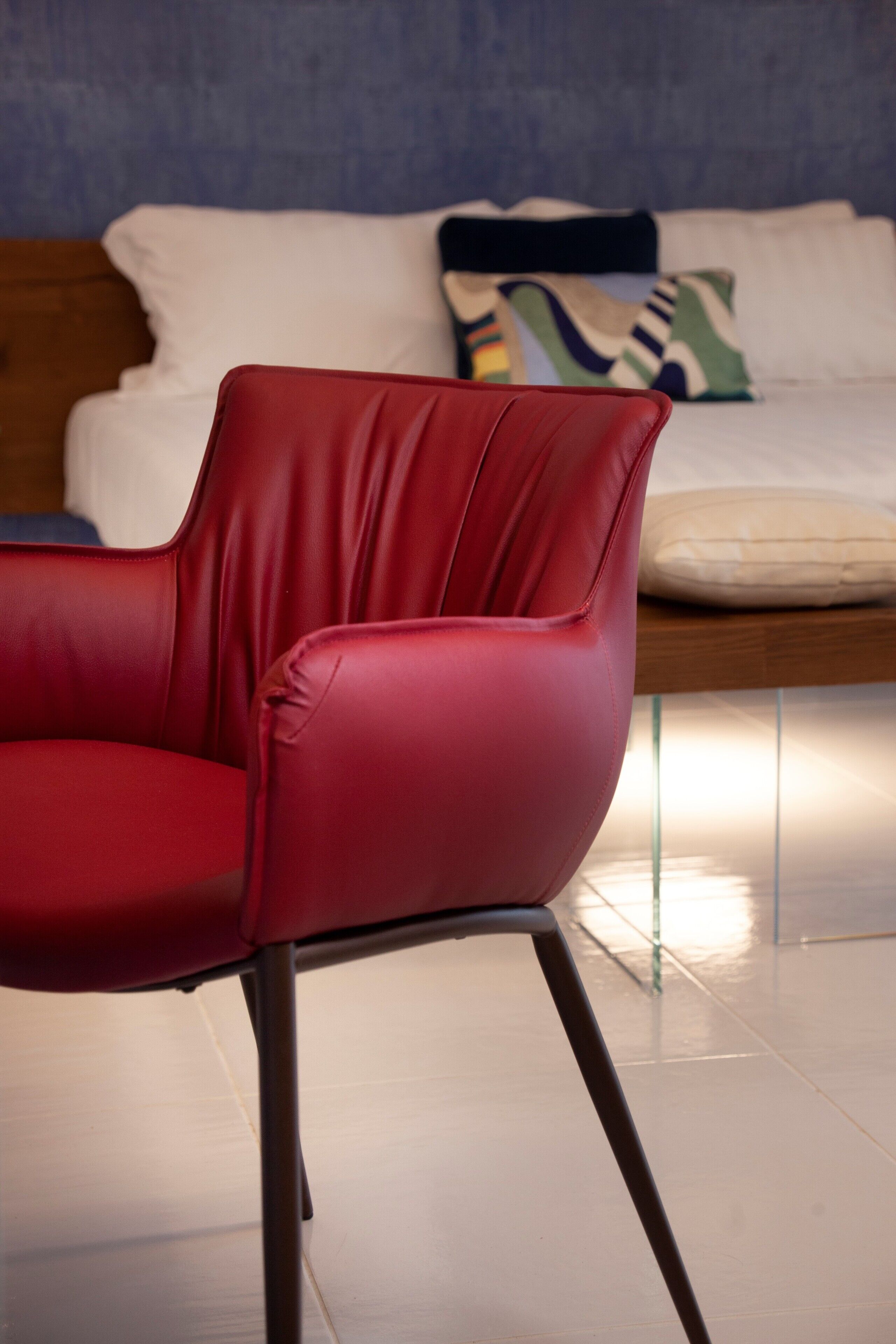 Una silla de cuero rojo en una habitación con una cama y almohadas al fondo.