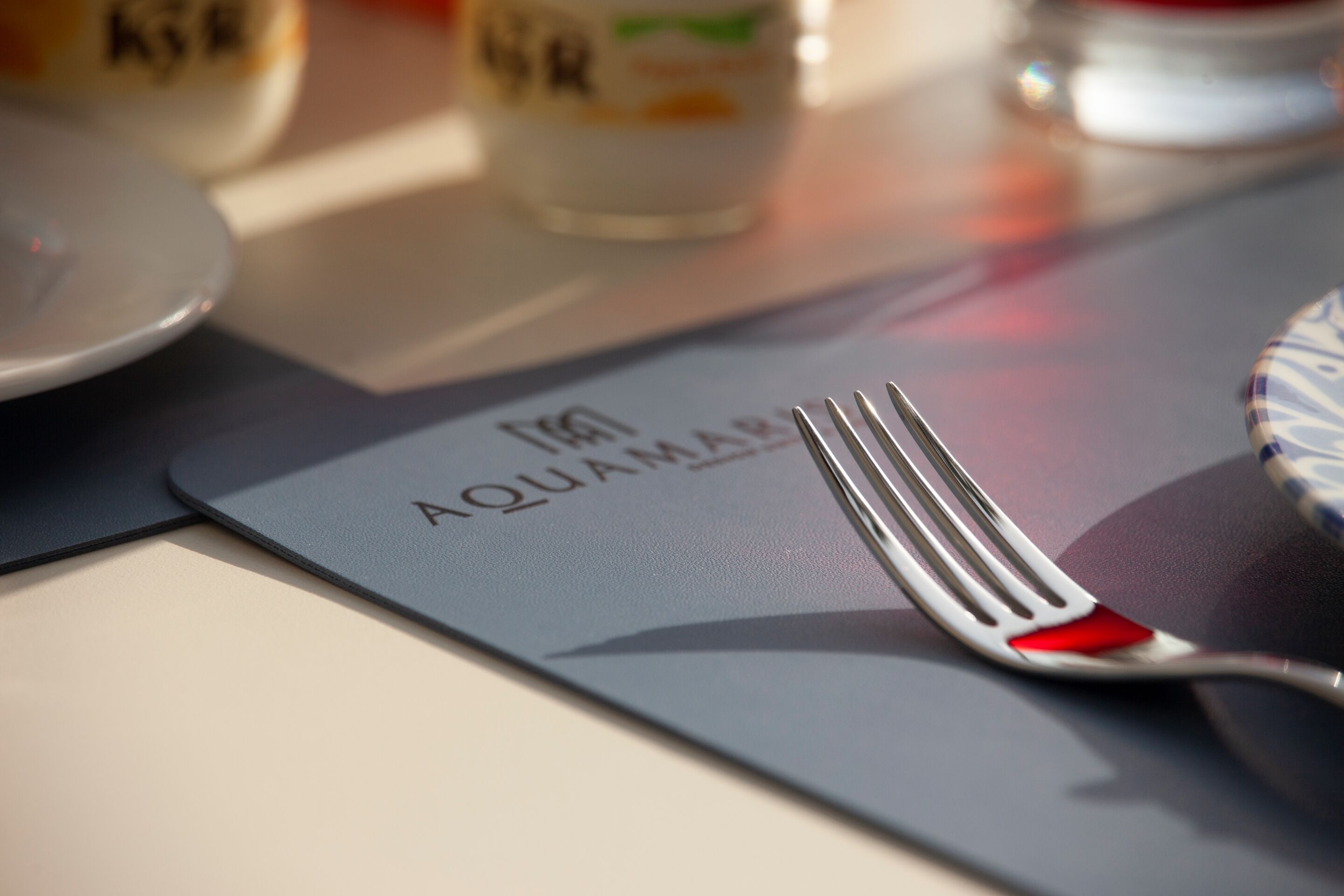 A dining table with a placemat labeled "AQUAMAS" and a fork on it.
