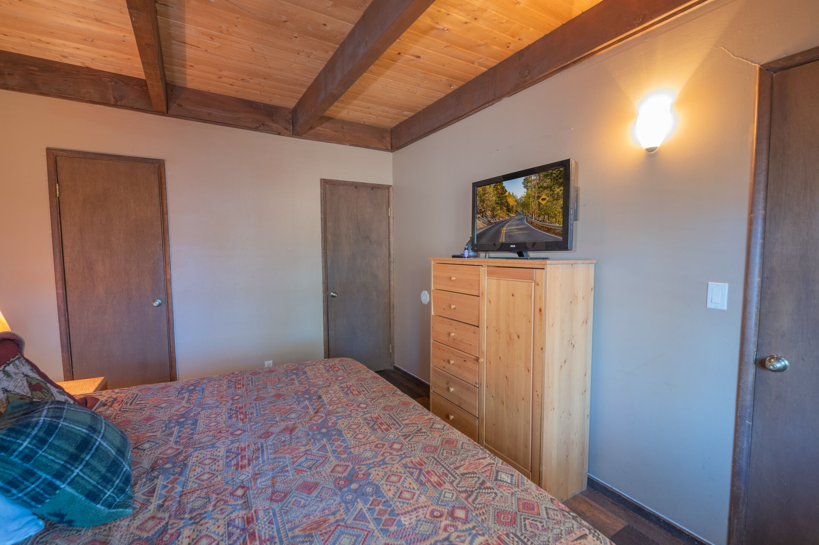 A bedroom with a bed, wooden wardrobe, and a wall-mounted TV.