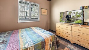 A bedroom with a bed, a dresser, a television, a window with blinds, and a framed picture on the wall.