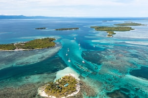 Vista aérea de una isla tropical con aguas turquesas cristalinas, varias islas pequeñas y barcos anclados en el agua.