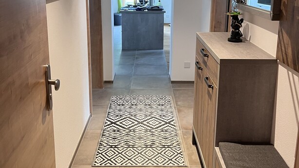 Un pasillo que conduce a una cocina con un alfombra estampado, armarios de madera y un perchero.