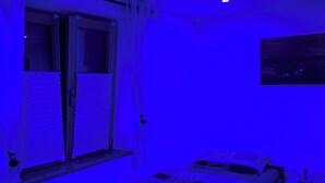 Una habitación con cama, mesita de noche, ventana con persianas y lámpara en el techo.