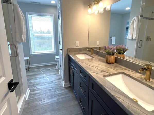 A bathroom with a double sink, dark cabinets, a large mirror, and a window with blinds.